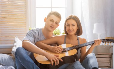 Aşık mutlu bir çift. Genç şık moda çiftimizin göz kamaştırıcı şehvetli portresi. Genç adam sevgili kızı için gitar çalıyor..
