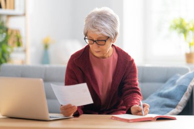 Elinde kağıt makbuzla kanepede oturan yaşlı kadın masrafları hesaplıyor, aile bütçesini yönetiyor..