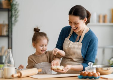 Mutlu aile birlikte fırın hazırlıyor. Anne ve kız çocuk kurabiye pişiriyor ve mutfakta eğleniyorlar. Ev yapımı yemek ve küçük bir yardımcı..    