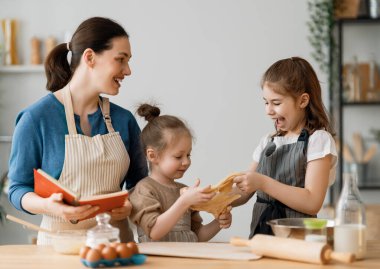 Mutlu aile birlikte fırın hazırlıyor. Anne ve çocuk kızları kurabiye pişiriyor ve mutfakta eğleniyorlar. Ev yapımı yemek ve küçük bir yardımcı..   