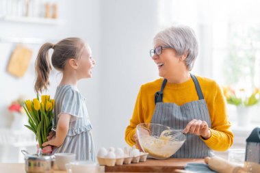 Mutlu aile birlikte fırın hazırlıyor. Küçük kız mutfakta büyükannesine çiçek veriyor.. 