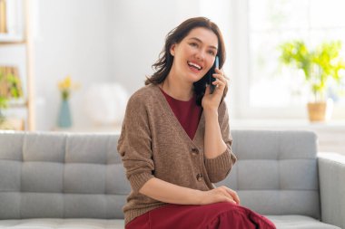 Mutlu, sıradan, güzel bir kadın evde bir koltukta telefonla konuşuyor..