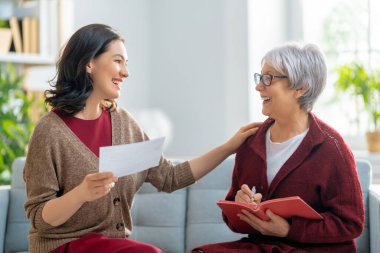 Elinde kağıt makbuzla kanepede oturan iki kadın, masrafları hesaplıyor, aile bütçesini yönetiyor..