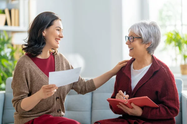 Elinde kağıt makbuzla kanepede oturan iki kadın, masrafları hesaplıyor, aile bütçesini yönetiyor..
