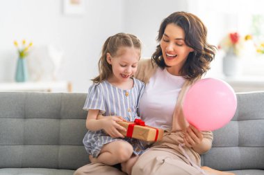 Anneler Günün kutlu olsun! Çocuk annesini tebrik ediyor. Anne ve kızı gülümsüyor ve hediyelerini tutuyorlar. Aile tatili ve birliktelik.