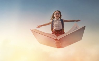 Okula dönün! Mutlu şirin, çalışkan çocuk günbatımı gökyüzünün arka planında kitabın üzerinde uçuyor. Eğitim ve okuma kavramı. Hayal gücünün gelişimi..