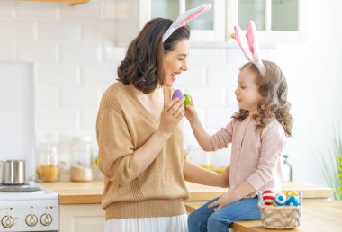 İyi tatiller! Bir anne ve kızı yumurta boyuyor. Aile Paskalya için hazırlanıyor. Sevimli küçük kız tavşan kulağı takıyor..