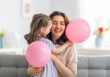 Anneler Günün kutlu olsun! Çocuk annesini tebrik ediyor. Anne ve kızı gülümsüyor ve hediyelerini tutuyorlar. Aile tatili ve birliktelik.