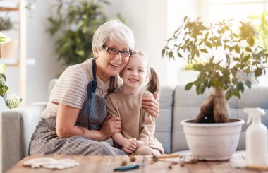Şirin bir kız çocuğu büyükannesinin bitkilere bakmasına yardım ediyor. Büyükanne ve torunu evde bahçe işleriyle uğraşıyorlar. Baharda mutlu bir aile.