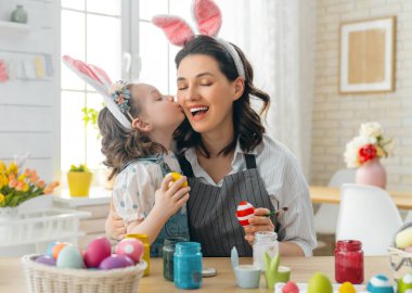 Anne ve kızı yumurta boyuyor. Mutlu aile Paskalya için hazırlanıyor. Tavşan kulağı takan şirin bir kız çocuğu..