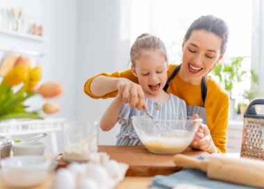 Mutlu aile birlikte fırın hazırlıyor. Anne ve kız çocuk kurabiye pişiriyor ve mutfakta eğleniyorlar. Ev yapımı yemek ve küçük bir yardımcı..     