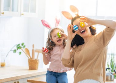 İyi tatiller! Yumurta boyayan bir anne ve kızı. Aile Paskalya için hazırlanıyor. Sevimli küçük kız tavşan kulağı takıyor..