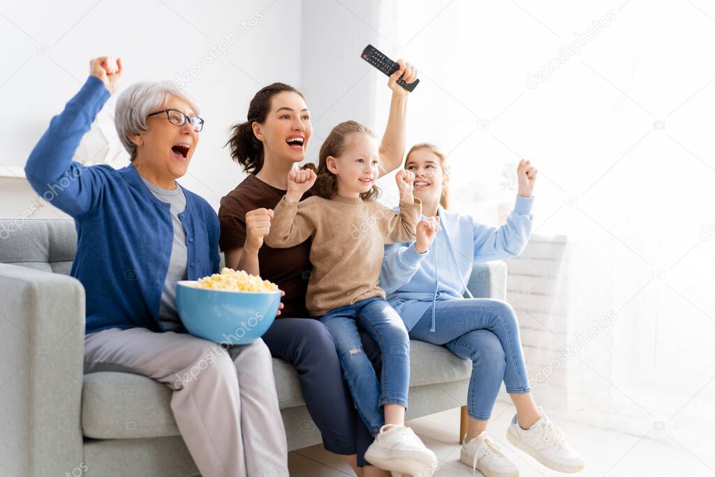 Happy family watching TV, movies with popcorn at home. Mother, daughters and grandmother spending time together.