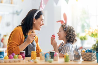 Anne ve kızı yumurta boyuyor. Mutlu aile Paskalya için hazırlanıyor. Tavşan kulağı takan şirin bir kız çocuğu..