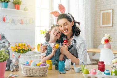 Anne ve kızı yumurta boyuyor. Mutlu aile Paskalya için hazırlanıyor. Tavşan kulağı takan şirin bir kız çocuğu..