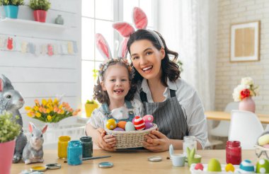 Anne ve kızı yumurta boyuyor. Mutlu aile Paskalya için hazırlanıyor. Tavşan kulağı takan şirin bir kız çocuğu..