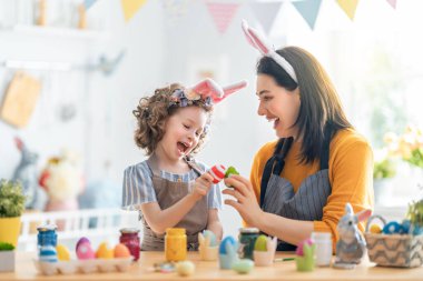 Anne ve kızı yumurta boyuyor. Mutlu aile Paskalya için hazırlanıyor. Tavşan kulağı takan şirin bir kız çocuğu..