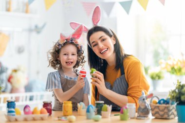 Anne ve kızı yumurta boyuyor. Mutlu aile Paskalya için hazırlanıyor. Tavşan kulağı takan şirin bir kız çocuğu..