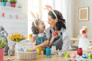 Anne ve kızı yumurta boyuyor. Mutlu aile Paskalya için hazırlanıyor. Tavşan kulağı takan şirin bir kız çocuğu..