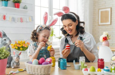 Anne ve kızı yumurta boyuyor. Mutlu aile Paskalya için hazırlanıyor. Tavşan kulağı takan şirin bir kız çocuğu..