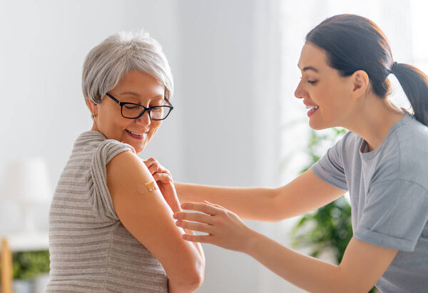 Старшая женщина после прививки и ее взрослая дочь дома. Защита от вирусов COVID-2019.