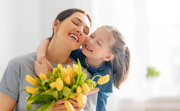 幸せな母親の日 子供の娘は母親を祝福し 彼女の花を与えます ママと女の子は笑顔で抱き合っている 家族の休日と友情 — ストック写真