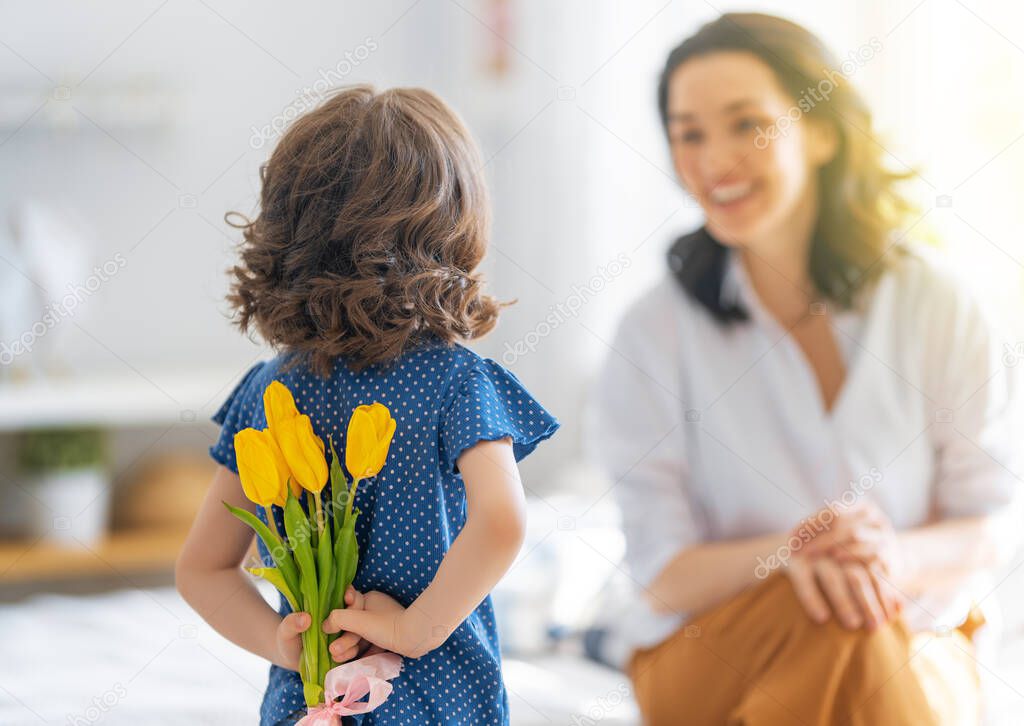 Happy mother's day. Child daughter congratulates mom and gives her flowers. Mum and girl smiling and hugging. Family holiday and togetherness.
