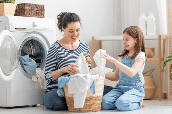 美しい若い女性と子供の女の子の小さなヘルパーは家で洗濯をしながら楽しさと笑顔を持っています — ストック写真