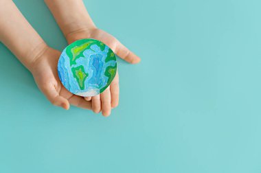 Child is holding planet in hands on teal background. Earth day holiday concept.