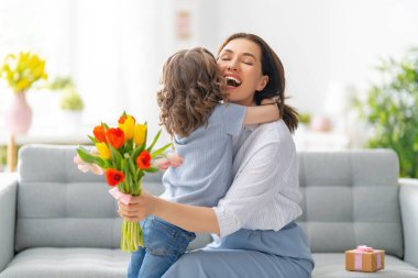 Anneler Günün kutlu olsun. Çocuk kızı annesini tebrik eder ve ona çiçek verir. Anne ve kız gülümsüyor ve sarılıyorlar. Aile tatili ve birliktelik.