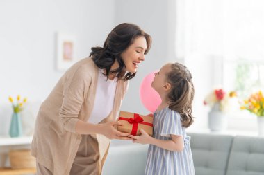 Anneler Günün kutlu olsun! Çocuk annesini tebrik ediyor. Anne ve kızı gülümsüyor ve hediyelerini tutuyorlar. Aile tatili ve birliktelik.