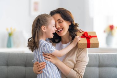 Anneler Günün kutlu olsun! Çocuk annesini tebrik ediyor. Anne ve kızı gülümsüyor ve hediyelerini tutuyorlar. Aile tatili ve birliktelik.