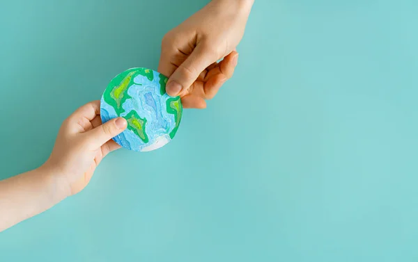 Child and adult holding planet in hands on teal background. Earth day holiday concept.