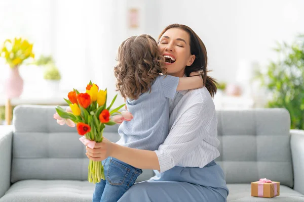 幸せな母親の日 子供の娘は母親を祝福し 彼女の花を与えます ママと女の子は笑顔で抱き合っている 家族の休日と友情 — ストック写真