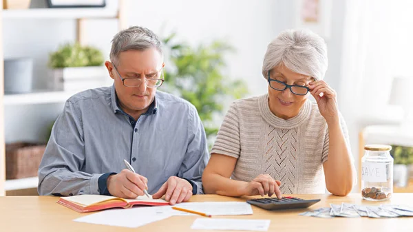高齢者の夫婦の机の上に紙の領収書を手に座って費用を計算し 家族の予算を管理している — ストック写真