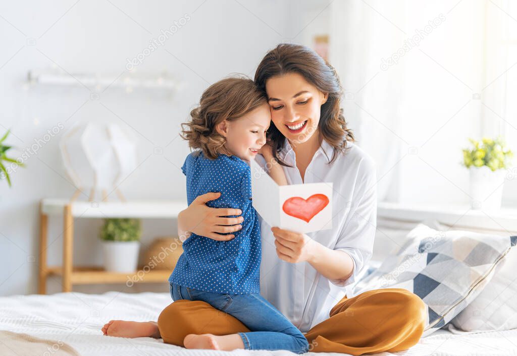 Happy mother's day! Child daughter is congratulating mom and giving her postcard. Mum and girl smiling and hugging. Family holiday and togetherness.