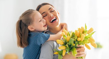 Anneler Günün kutlu olsun. Çocuk kızı annesini tebrik eder ve ona çiçek verir. Anne ve kız gülümsüyor ve sarılıyorlar. Aile tatili ve birliktelik.