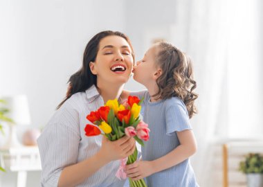 Anneler Günün kutlu olsun. Çocuk kızı annesini tebrik eder ve ona çiçek verir. Anne ve kız gülümsüyor ve sarılıyorlar. Aile tatili ve birliktelik.