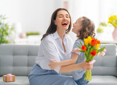 Anneler Günün kutlu olsun. Çocuk kızı annesini tebrik eder ve ona çiçek verir. Anne ve kız gülümsüyor ve sarılıyorlar. Aile tatili ve birliktelik.