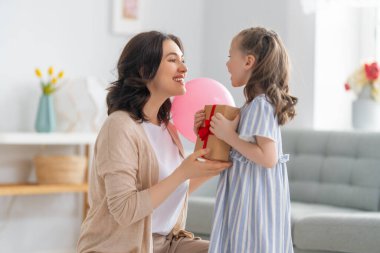 Anneler Günün kutlu olsun! Çocuk annesini tebrik ediyor. Anne ve kızı gülümsüyor ve hediyelerini tutuyorlar. Aile tatili ve birliktelik.