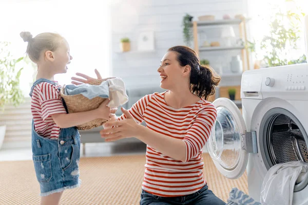 美しい若い女性と子供の女の子の小さなヘルパーは家で洗濯をしながら楽しさと笑顔を持っています — ストック写真