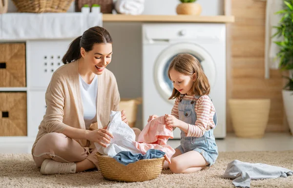 美しい若い女性と子供の女の子の小さなヘルパーは家で洗濯をしながら楽しさと笑顔を持っています — ストック写真
