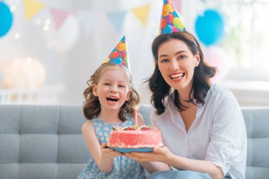 Çocuk pastanın üzerindeki mumları üflüyor. Anne ve kızı doğum gününü kutluyorlar..