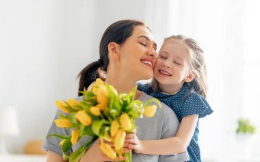 Anneler Günün kutlu olsun. Çocuk kızı annesini tebrik eder ve ona çiçek verir. Anne ve kız gülümsüyor ve sarılıyorlar. Aile tatili ve birliktelik.