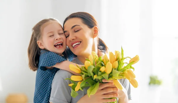 幸せな母親の日 子供の娘は母親を祝福し 彼女の花を与えます ママと女の子は笑顔で抱き合っている 家族の休日と友情 — ストック写真