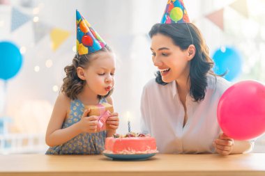 Çocuk pastanın üzerindeki mumları üflüyor. Anne ve kızı doğum gününü kutluyorlar..