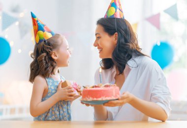 Çocuk pastanın üzerindeki mumları üflüyor. Anne ve kızı doğum gününü kutluyorlar..