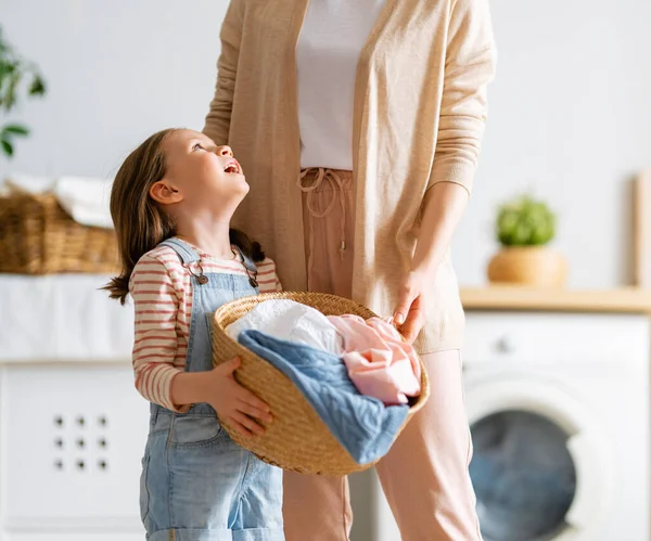 美しい若い女性と子供の女の子の小さなヘルパーは家で洗濯をしながら楽しさと笑顔を持っています — ストック写真