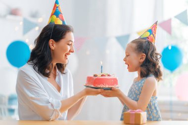 Çocuk pastanın üzerindeki mumları üflüyor. Anne ve kızı doğum gününü kutluyorlar..