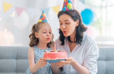 Çocuk pastanın üzerindeki mumları üflüyor. Anne ve kızı doğum gününü kutluyorlar..